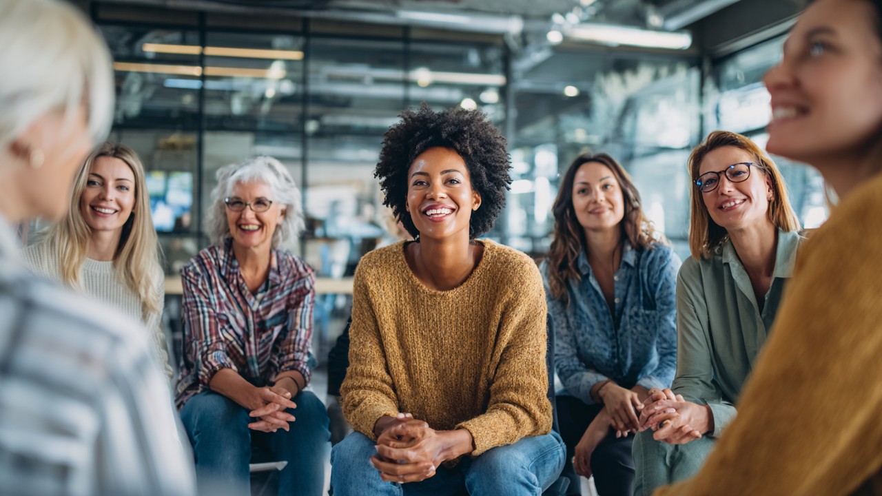 Diverse group of professional men and women discussing gender equality and inclusive leadership in a corporate meeting room with positive, collaborative body language.