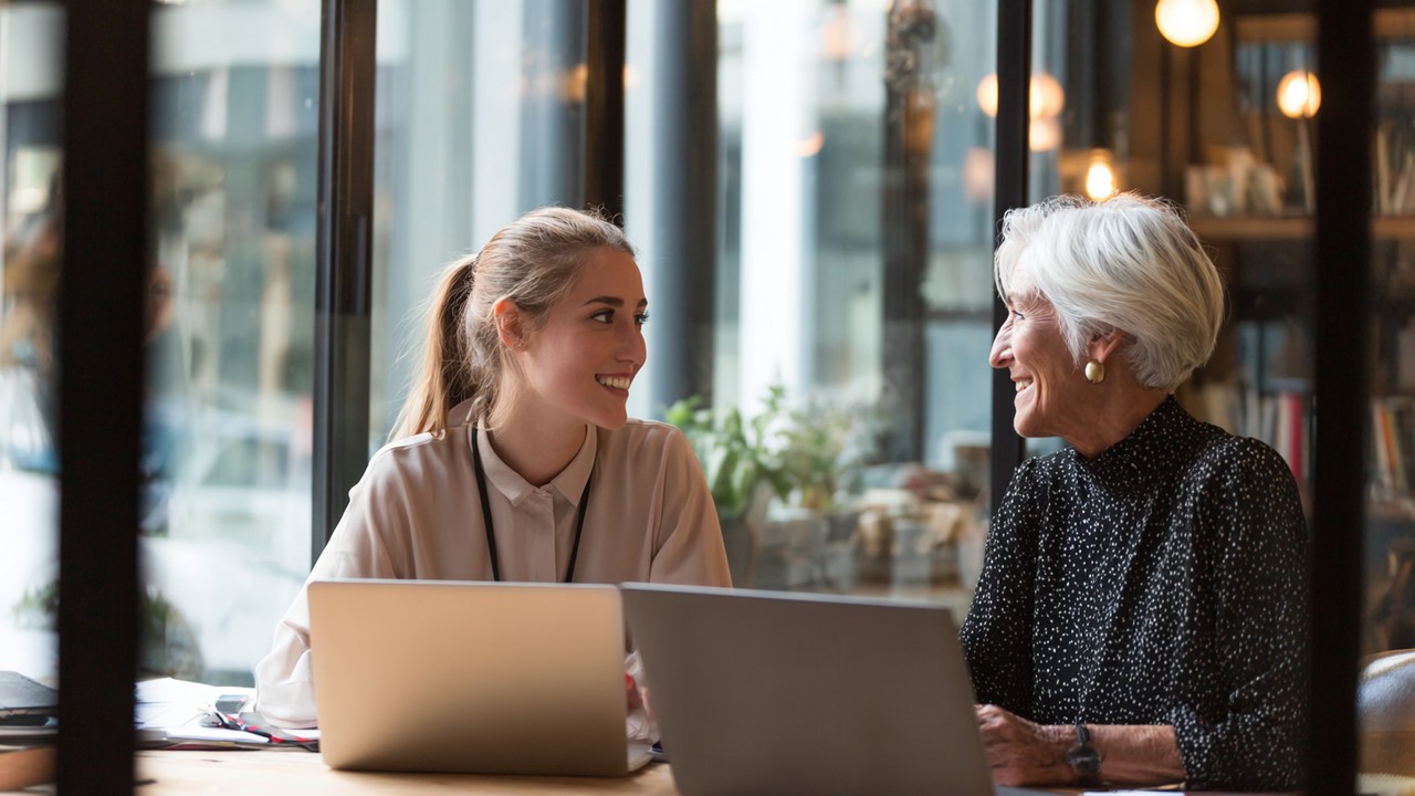 Confident female entrepreneur receiving mentorship from experienced business mentor in a cozy office with laptops and notebooks.