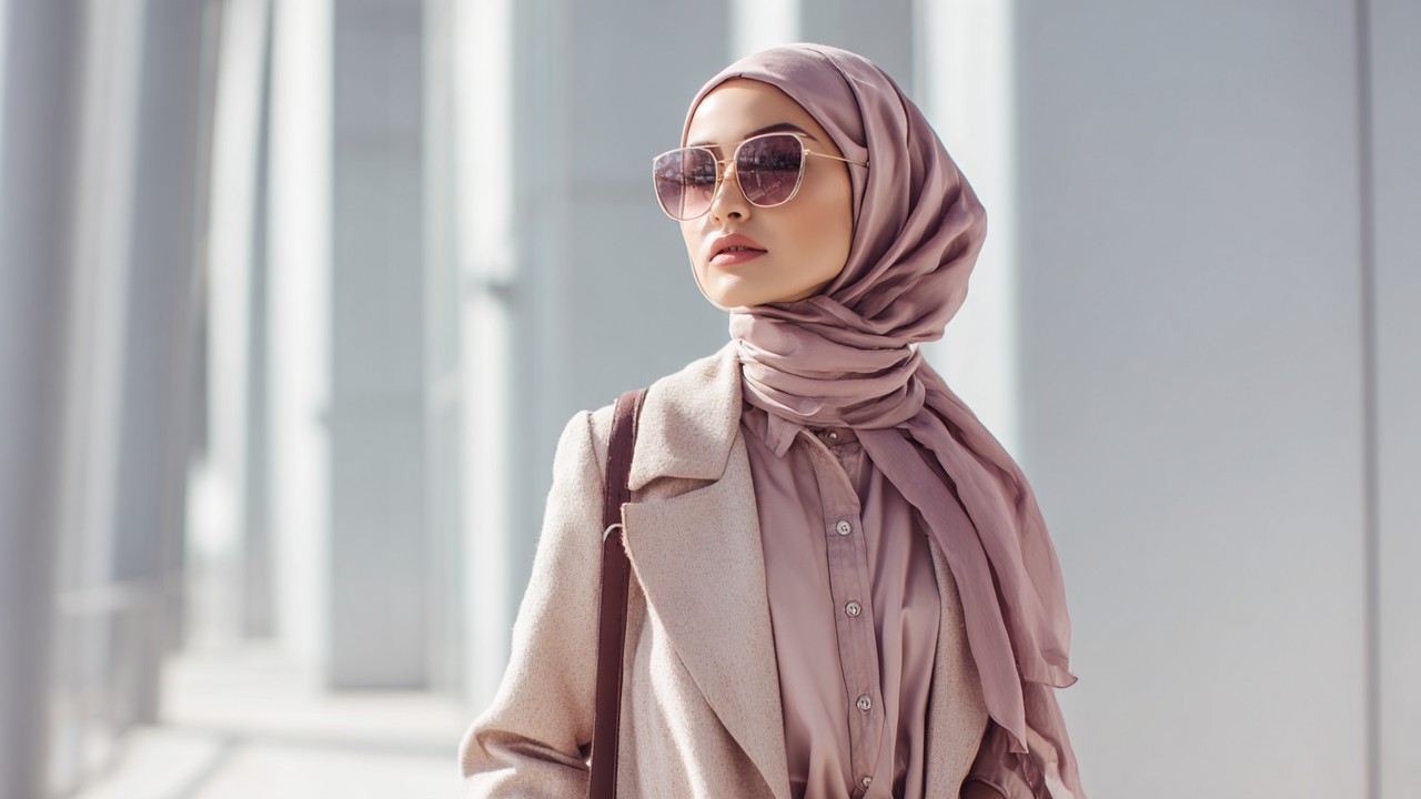 Stylish young woman in modern tesettür fashion with neutral tones, standing confidently in a bright urban setting, showcasing Turkish modest style trends 2025.
