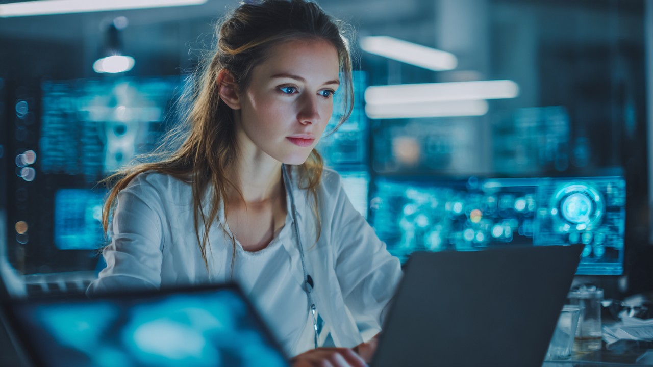 Young female entrepreneur working on a laptop in a futuristic, tech-savvy workspace with digital devices and interfaces, symbolizing female leadership in digital business.