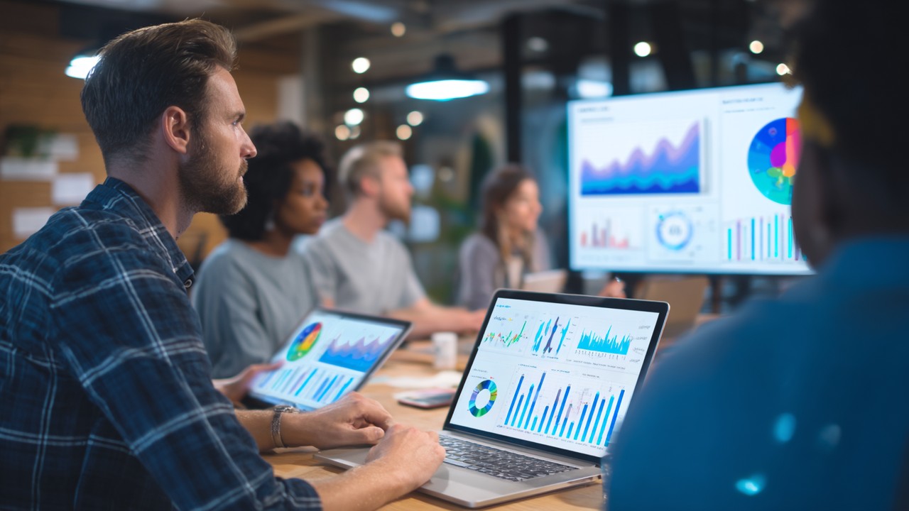 Modern ofis ortamında farklı kişiler, dizüstü ve tabletlerle web analitiği ve SEO başarısı için veri odaklı optimizasyon yaparken grafikler ve tablolar gösteriyor.