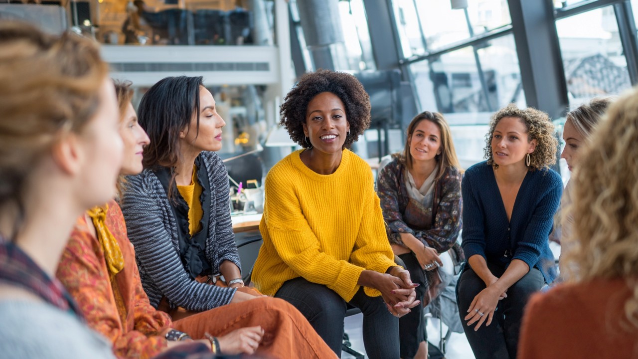 Modern ofis ortamında, mentorluk yapan kadın liderler ve genç kadınlar, güçlendirme ve kadın liderliği temalı ilham verici çalışma ortamı.
